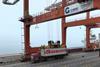An OOCL truck sits beneath a large crane as its container is loaded