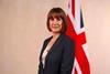 The image shows Rachel Reeves dressed in a grey suit standing in front of the Union Jack flag