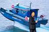 Yinson GreenTech employee standing in front of an image of the Hydroglyder fully electric hydrofoil