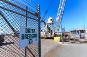 A Dutra dredging sign on a fence with a crane behind