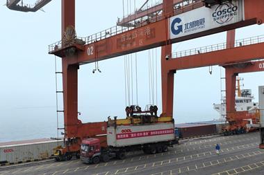An OOCL truck sits beneath a large crane as its container is loaded