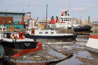 An African port. A large amount of solid waste floats on the surface of the water around the ships.