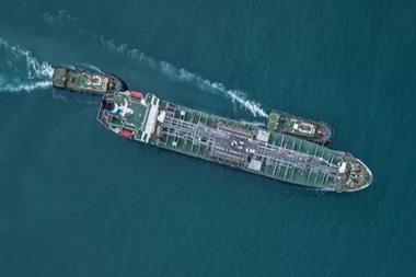 An aerial shot of a cargo ship at sea with two tugs