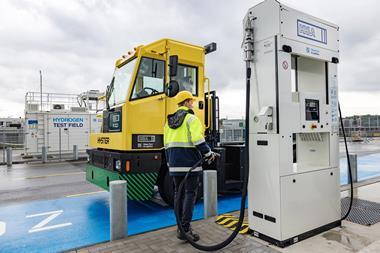 The image shows a Hyster hydrogen fuel cell-powered terminal tractor in action at HHLA