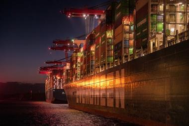 The image shows a ship berthed at a lit up dock at night