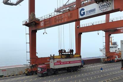 An OOCL truck sits beneath a large crane as its container is loaded