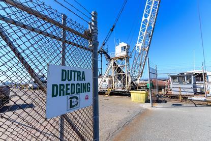 A Dutra dredging sign on a fence with a crane behind