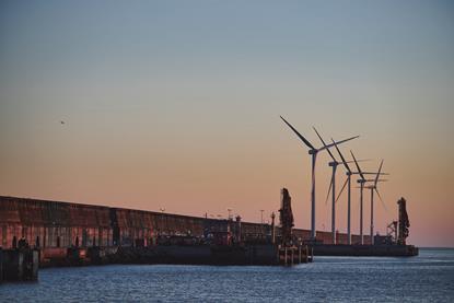 The image shows Bilbao Port by sunset with wind turbines in the background