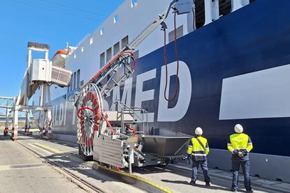 The image shows two operators checking the OPS cabling management system to ensure the connection to the ship quayside