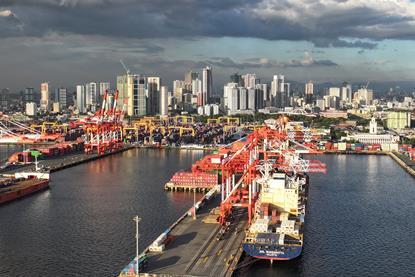 Manila South Harbour, Philippines, showing ships portside, a number of ship-to-shore cranes and high rise buildings in the background