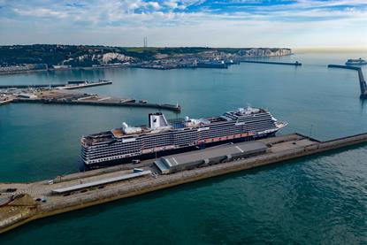 The pictures shows a Holland America Line cruise ship against a backdrop of the White Cliffs of Dover