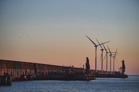 The image shows Bilbao Port by sunset with wind turbines in the background