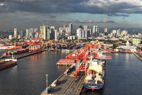Manila South Harbour, Philippines, showing ships portside, a number of ship-to-shore cranes and high rise buildings in the background