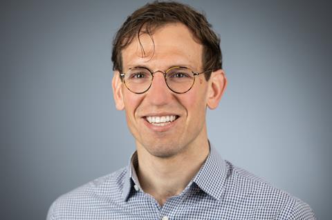 A picture of Cameron Gook, a white man wearing glasses and a blue shirt