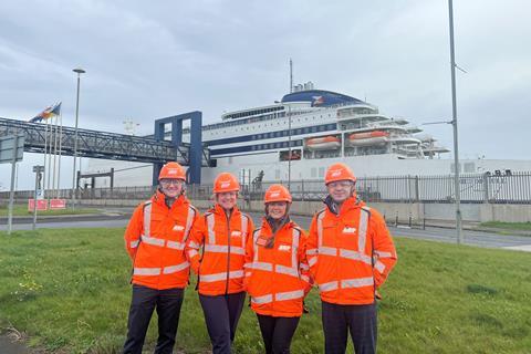 A group of people in orange jackets and helmets standing in front of a large ship in Hull